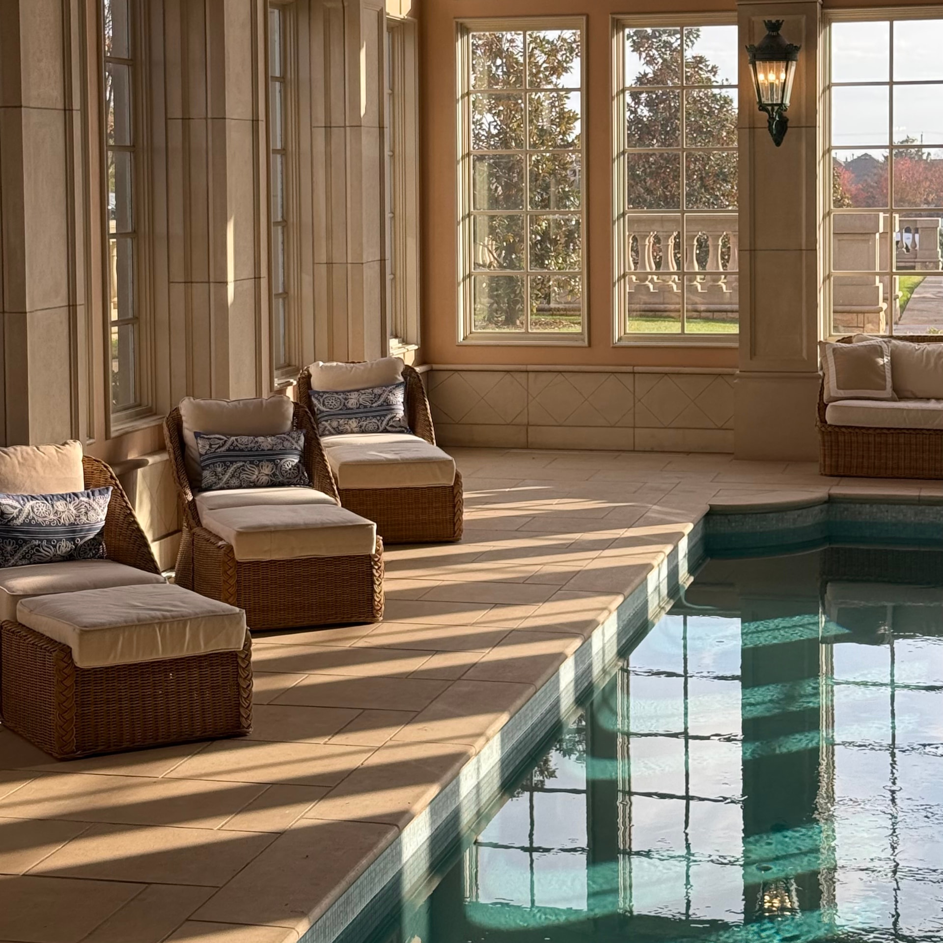 Sunlit indoor pool lounge with wicker seating and tall windows