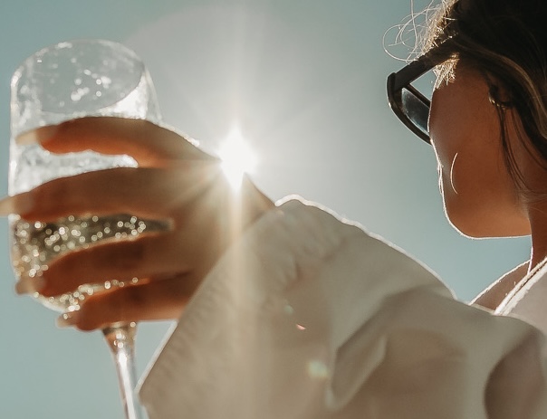 Woman in sunglasses holding a sparkling glass against bright sunlight